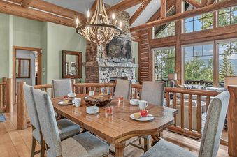 A rustic dining area with a wooden table set for a meal, surrounded by upholstered chairs.