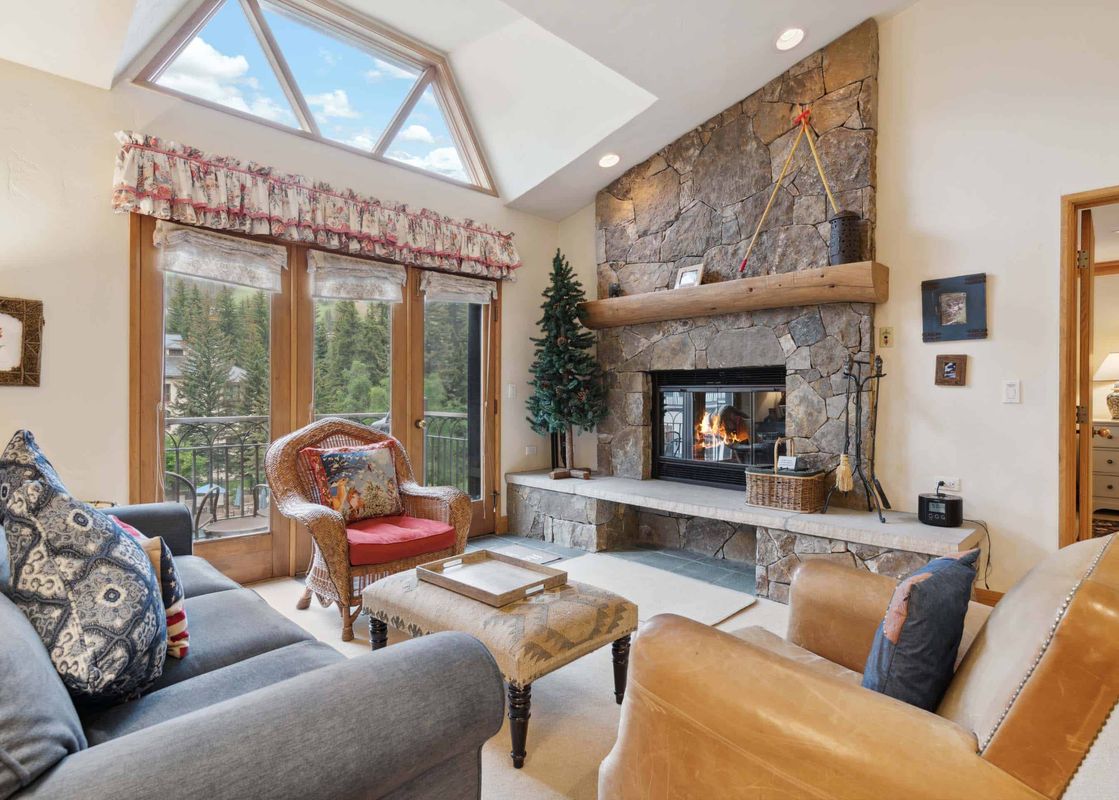 A cozy lounge area at The Charter E430 with a rustic stone fireplace, comfortable seating, and large windows looking out onto evergreen trees.