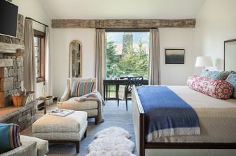 A cozy bedroom at Four Pines 14 features a large bed, a desk with an exterior view, a comfortable seating area, and a stone fireplace.