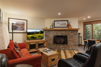 A cozy living room at Terracehouse 63 with an orange sofa, a television, a stone fireplace, and a dining area with a view of trees.