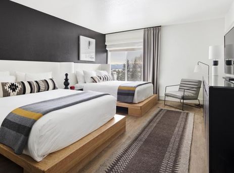 Modern hotel room with two queen beds and a large window looking out at snowy trees.