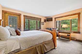 Cozy bedroom in Snowridge 6 with a wooden bed frame, large windows looking out to trees, and a mountain lodge aesthetic.