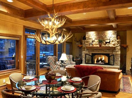 A rustic and cozy dining and living area at Ski Vista Penthouse featuring a stone fireplace and antler chandelier.