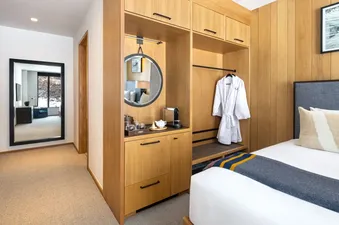 The Sylvan Lodge Double Guest Room interior showing a full-length mirror, a built-in coffee station, a closet with a white bathrobe, and a corner of a neatly made bed.