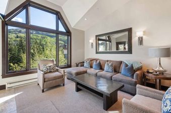 A spacious living area at The Charter B440 features a large L-shaped sofa, an armchair, and a coffee table, all set against a backdrop of floor-to-ceiling windows with mountain views.