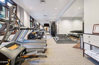 Fitness center in The Aspen 12B with modern treadmills, ellipticals, dumbbells, and benches.