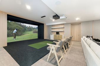 A luxury indoor golf simulator room with a large screen displaying a golf course, comfortable seating, and modern interior design at Kestrel at the Colony.