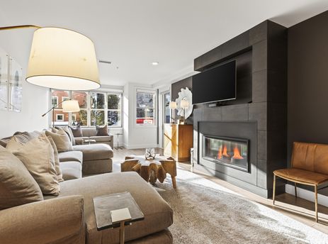 A modern living room features a large sectional sofa, a unique wooden coffee table, and a dark fireplace with a mounted television.