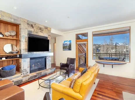 A spacious and inviting living room featuring a cozy stone fireplace, comfortable yellow leather sofa, and large windows offering stunning mountain views.