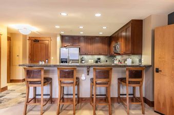 Kitchen with dark wood cabinets and a stainless steel refrigerator, with a breakfast bar that has four wooden stools and a granite countertop.