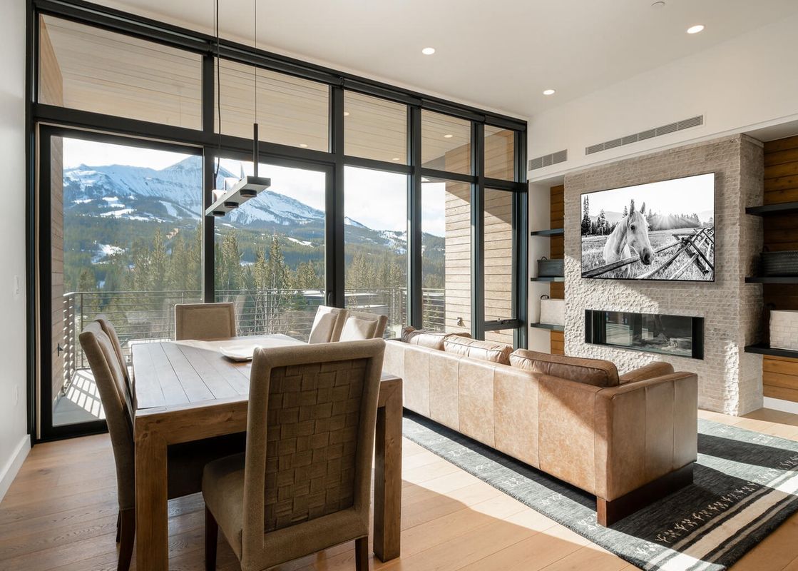 The interior of Moonlight Basin 204 Lakelodge features a large picture window offering a mountain view, a leather sofa with a contemporary fireplace, and a dining table with chairs.