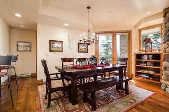 The dining area at Chateau Chamonix CX325 features a dark wood table with chairs and a bench, a chandelier, and a patterned area rug, creating a warm and inviting space.
