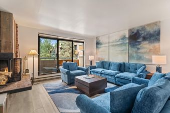 A view of the living room at Riverview Unit 22 featuring blue seating, a fireplace, and a balcony view.