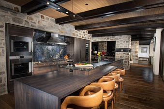 The kitchen at White Pine Canyon features a spacious island with bar seating, stainless steel appliances, a wood-burning fireplace, and a gorgeous stone wall.