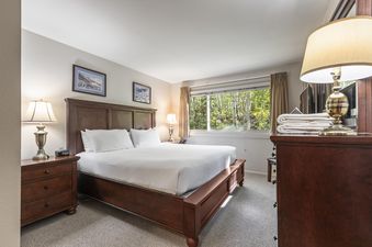 The primary bedroom at Snow Flower 135 Park City, featuring a king-sized bed with a wooden frame, bedside tables, lamps, and a window overlooking a vibrant forest.