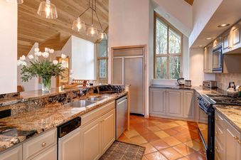 A spacious, well-lit kitchen with granite countertops, stainless steel appliances, and a vaulted wood ceiling.