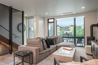 A modern and inviting living room in Canton House featuring a large sectional sofa, a wooden coffee table, a sleek fireplace, and expansive windows with a view of the outdoors.