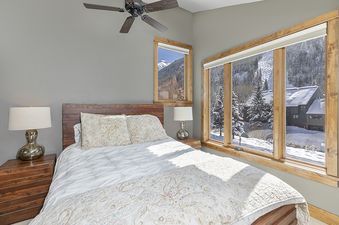 A bedroom with a king-sized bed and a view of the snowy mountains outside the window.