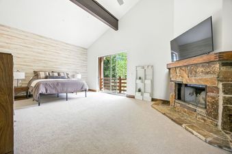 A spacious master bedroom with a king-sized bed, a stone fireplace, and a private balcony overlooking green trees.