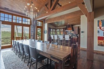 A luxurious dining room in Alpine Sanctuary features a long wooden table and scenic views.
