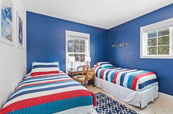The twin bedroom features two beds with red, white, and blue striped bedding, a wooden desk with two lamps, and bright blue walls.
