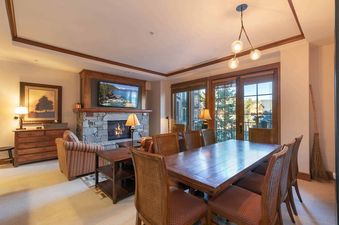 A spacious living room with a fireplace, large windows with a view of the snow-covered mountains, and a dining table set for six.