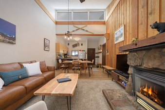 A spacious living area featuring a comfortable brown leather couch, a rustic wooden coffee table, and a large stone fireplace with a television set to the side.