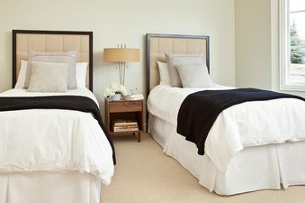 A twin bedroom at Pines Garden 4050 featuring two beds with white linens, black throws, upholstered headboards, and a shared nightstand with a lamp and flowers.