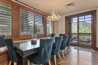 The dining area at Silver Strike Lodge 407 with a dark wood table, teal chairs, and mountain views from the window and balcony.