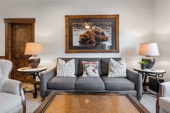 A cozy living room at The Charter D3205 with a gray sofa, decorative pillows, elegant lamps, and a large framed artwork of bears.