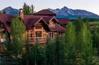 An exterior view of the luxury Evergreen log cabin nestled in lush green forests with mountain peaks in the background.