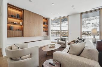 A modern living room in Founders Place 2304 with a fireplace, comfortable seating, and a view of a snowy landscape through large windows.