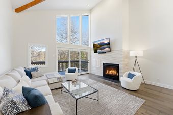 A spacious and modern living room at Winterlight at Snow Park with a sectional sofa, glass coffee table, fireplace, and large windows offering a winter view.