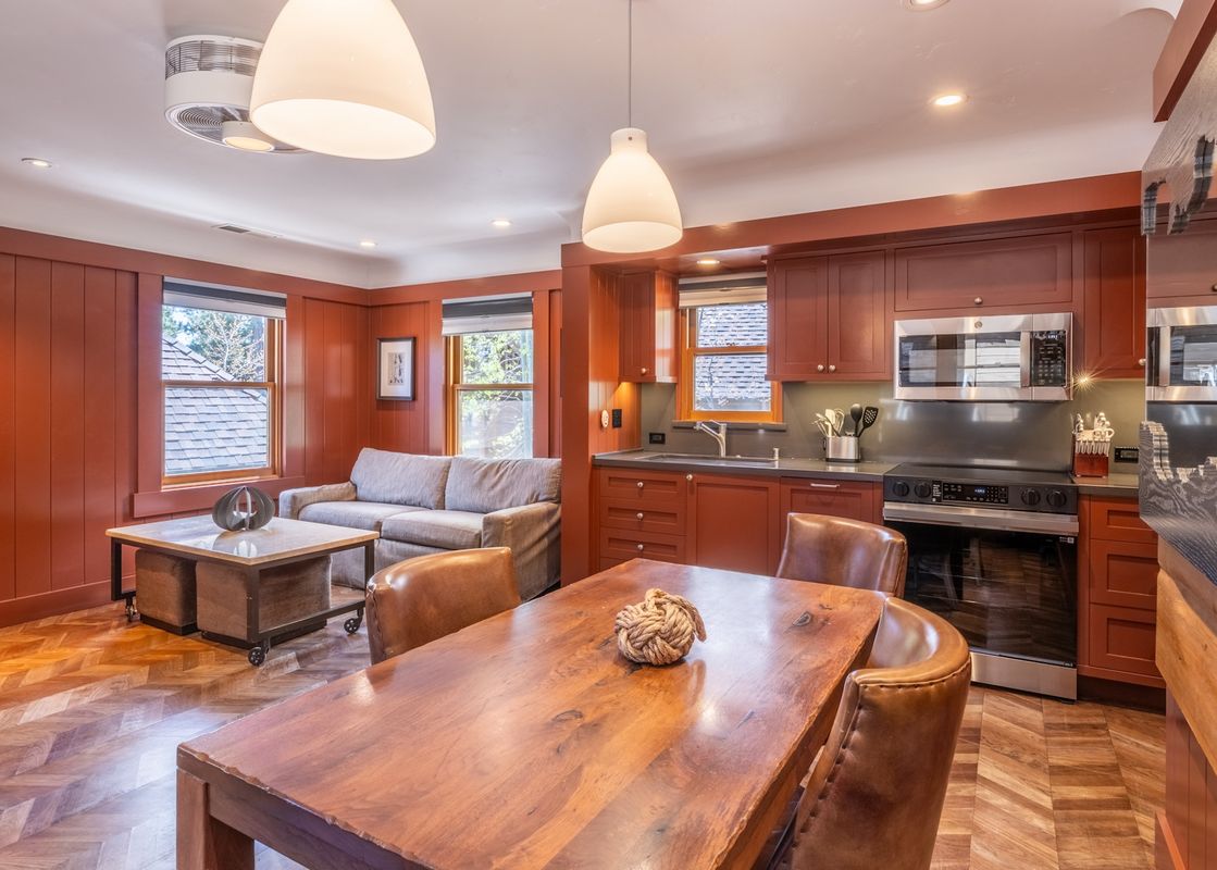 An open-concept living area and kitchen with warm wood paneling, a gray sofa, a wooden dining table, and stainless steel appliances.