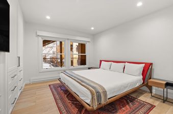 A bedroom with a large bed, two windows, and a wooden floor.