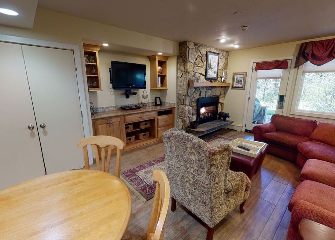 The living room of Manor Vail 081 features a fireplace with a stone surround, a red sectional sofa, an armchair, a coffee table and a dining table with four chairs.