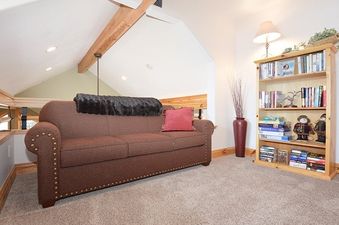 A cozy brown sofa with a dark throw blanket and a red pillow sits on a carpeted floor, accompanied by a wooden bookshelf filled with books and decorations.