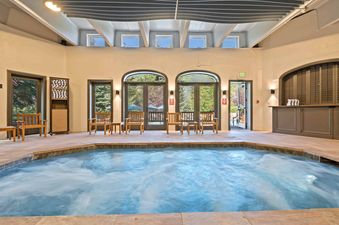 An inviting indoor hot tub area at The Charter B1305, featuring a bubbling hot tub surrounded by arching windows, wooden chairs, and unique architectural ceiling details.