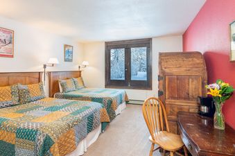 A bright bedroom in Manitou Lodge 2 features two beds with colorful quilts and a window overlooking snow-covered trees.