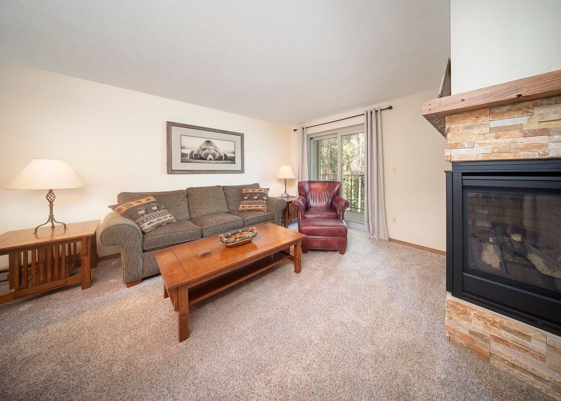 A cozy living room at Beaver Village 1123 features a comfortable sofa and armchair, a coffee table, and a fireplace, with a window offering a view of the outdoors.
