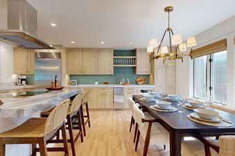 Modern open-plan kitchen and dining room at Windriver 2 with light wood cabinets, green backsplash, and a dining table set for six.
