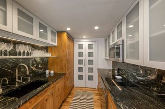 A modern galley kitchen at Chateau Beaver Creek Residence 203 features dark marble countertops, light wood lower cabinets, frosted glass upper cabinets, and a stainless steel sink with an integrated microwave.