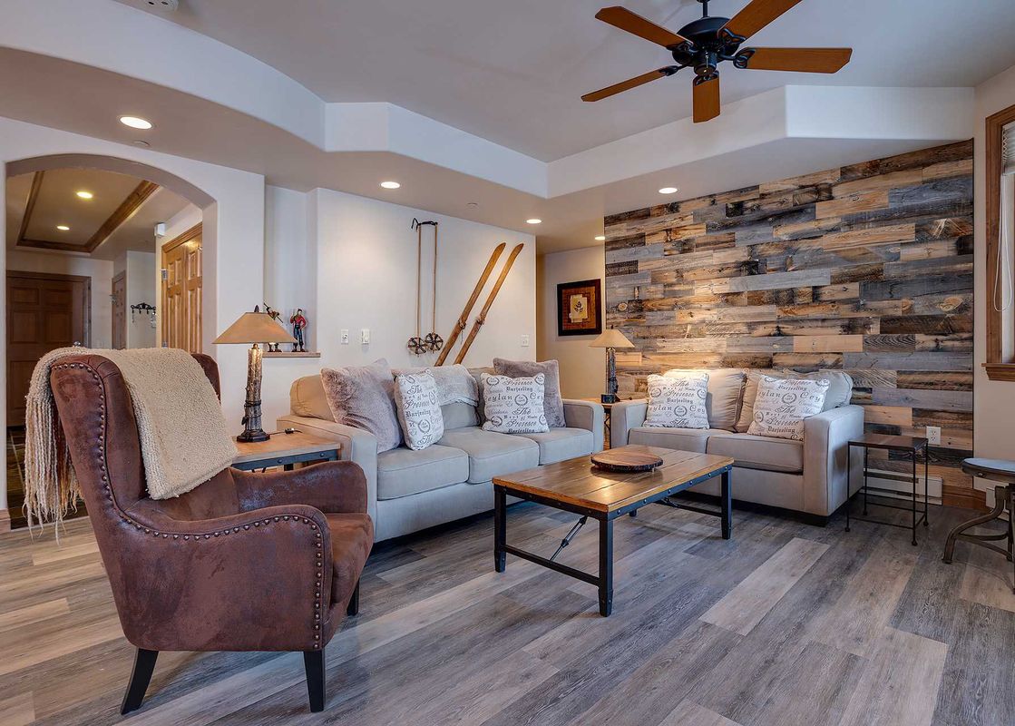 The living area of Chateau Chamonix CX326 features a brown leather armchair, two sofas with decorative pillows, a wooden coffee table, and a unique reclaimed wood accent wall, creating a cozy and rustic ambiance.