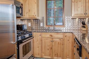 The kitchen of Moonlight Basin Lodging 38A Cowboy Heaven with wood cabinets and a stainless steel refrigerator, oven, and range, along with a tile floor.
