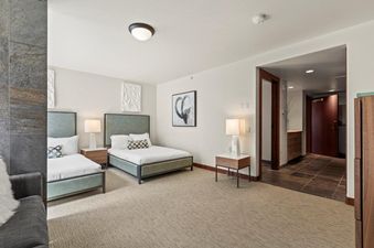 A modern bedroom at Lowell 401A with two queen beds, elegant bedside tables, and contemporary decor, leading into a hallway.