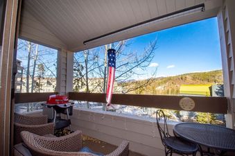 The Snowblaze C24 unit features a cozy balcony with outdoor seating, a grill, and a picturesque view of the surrounding mountains and buildings.