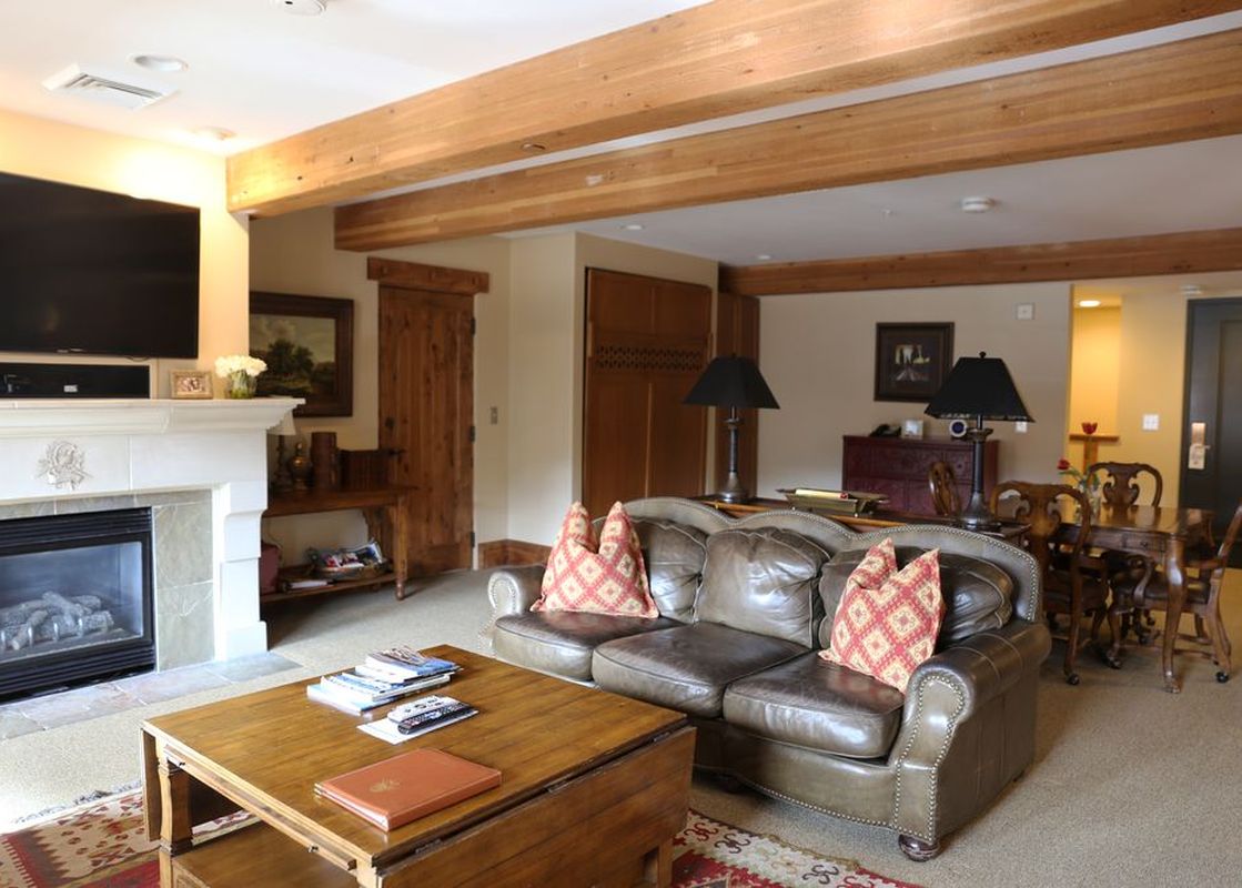 A comfortable brown leather sofa with red patterned pillows sits in a living room with a fireplace and wooden accents.