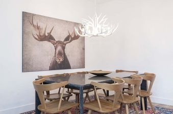 The dining area featuring a large table, wooden chairs, an antler chandelier, and a prominent moose portrait.