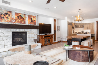 The living room of 132 Two Bedroom Black Diamond Lodge features a fireplace, a large flat-screen TV, and an antler chandelier.