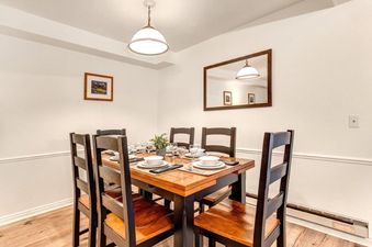A cozy dining area at Suncreek A7 with a wooden table set for six, featuring a central pendant light and a wall mirror reflecting the room.